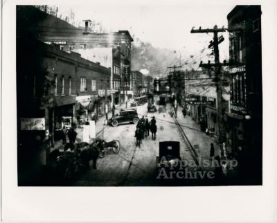 A town [Hazard] street filled with people, horses, and cars