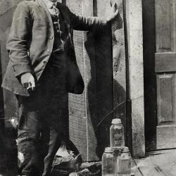 Man standing outside building with moonshine at his feet