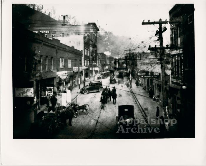 A town [Hazard] street filled with people, horses, and cars