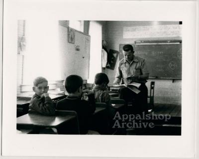Production still of three children and a teacher in a classroom - Kingdom Come School